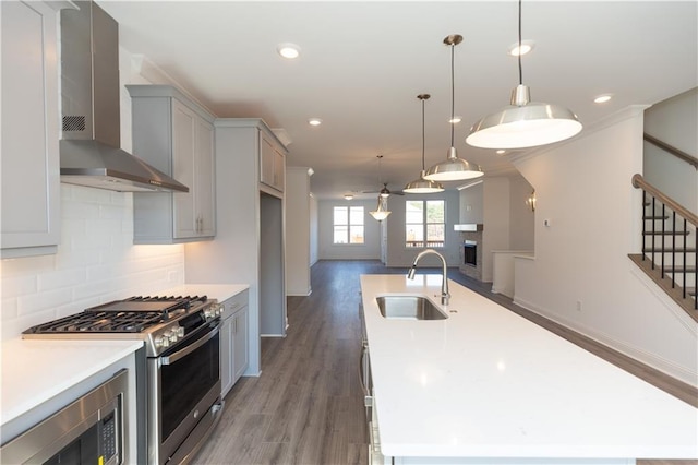 kitchen with gray cabinets, a center island with sink, stainless steel appliances, sink, and wall chimney range hood