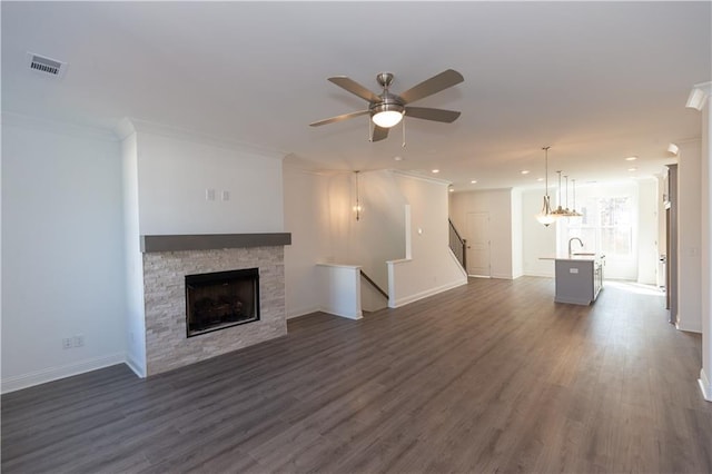 unfurnished living room featuring dark wood-type flooring, ornamental molding, a fireplace, ceiling fan, and sink