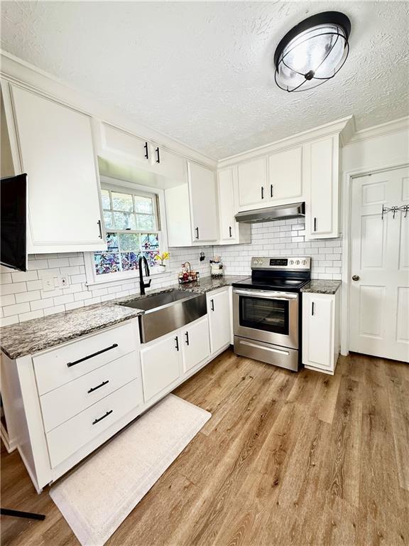 5347 Ocarol Ct, Stone Mountain, GA 30088 - kitchen featuring stainless steel range with electric stovetop, under cabinet range hood, a textured ceiling, light wood-type flooring, and white cabinets