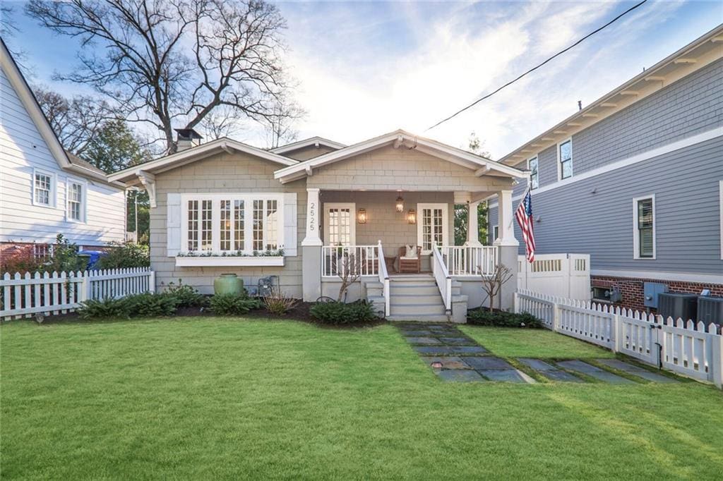 bungalow-style home featuring a front lawn, covered porch, fence, and central AC unit