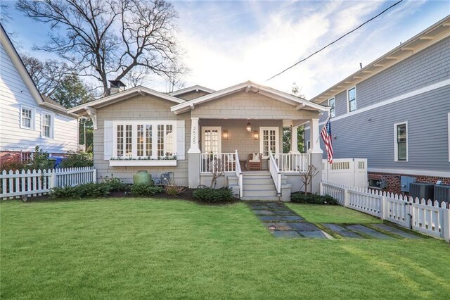 bungalow-style home featuring a front lawn, covered porch, fence, and central AC unit