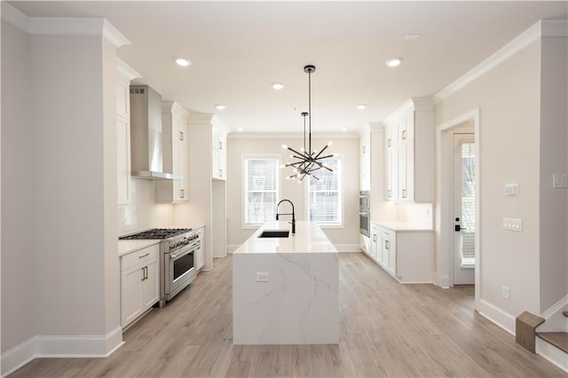 kitchen featuring wall chimney exhaust hood, decorative light fixtures, stainless steel appliances, a kitchen island with sink, and white cabinets