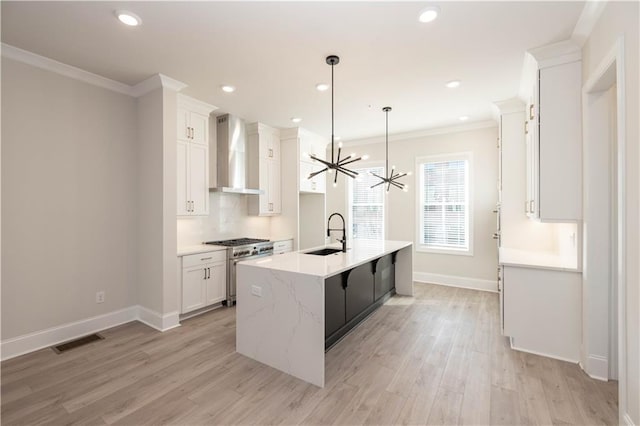 kitchen with decorative light fixtures, high end stove, white cabinetry, sink, and wall chimney range hood