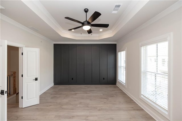 empty room featuring ornamental molding, light hardwood / wood-style floors, a raised ceiling, and ceiling fan