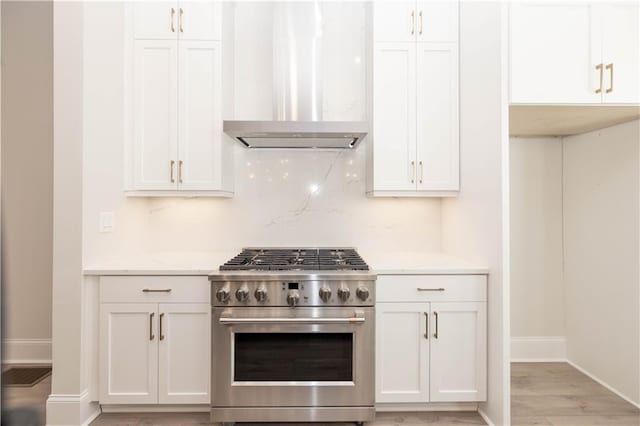 kitchen with white cabinetry, wall chimney range hood, high end stainless steel range, and backsplash