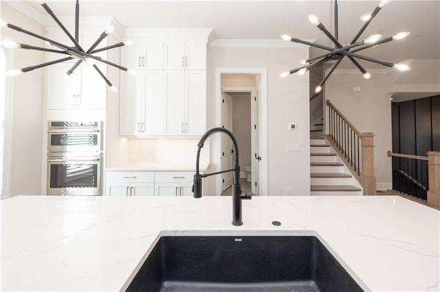 kitchen with sink, stainless steel double oven, light stone counters, and an inviting chandelier