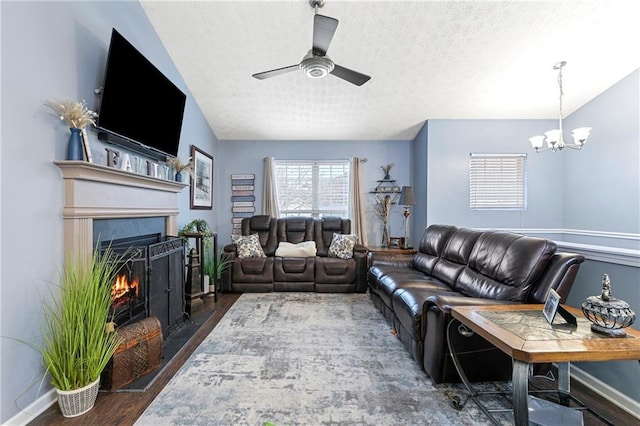 living room with ceiling fan with notable chandelier, dark wood-type flooring, and a textured ceiling