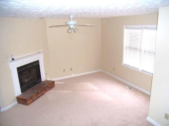 unfurnished living room with a brick fireplace, a textured ceiling, carpet floors, and ceiling fan