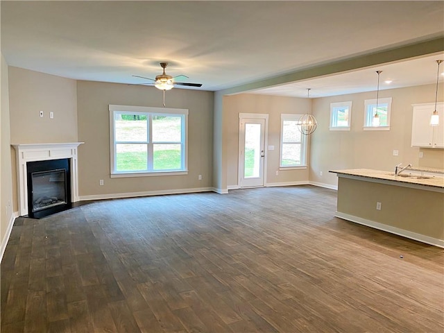 unfurnished living room featuring a ceiling fan, baseboards, dark wood-style floors, and a sink