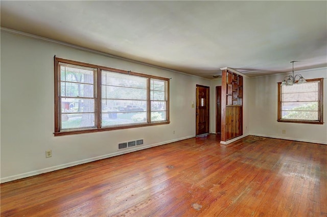 spare room featuring a healthy amount of sunlight, crown molding, visible vents, and wood finished floors