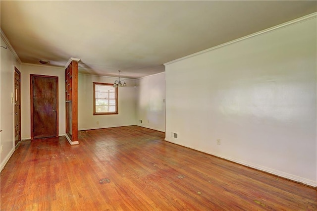 empty room with baseboards, ornamental molding, visible vents, a chandelier, and wood finished floors