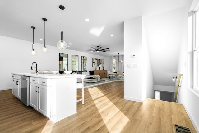 kitchen with a breakfast bar, pendant lighting, stainless steel dishwasher, light hardwood / wood-style floors, and a center island with sink