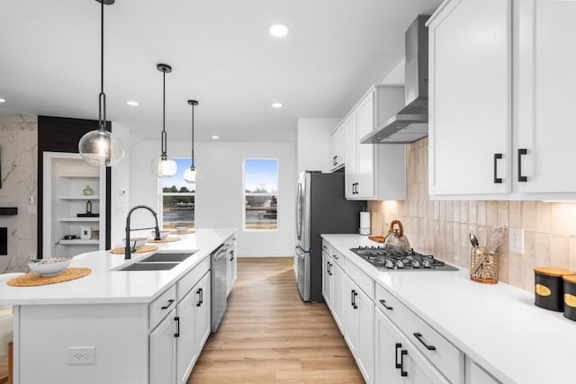 kitchen featuring wall chimney range hood, stainless steel appliances, sink, and white cabinets