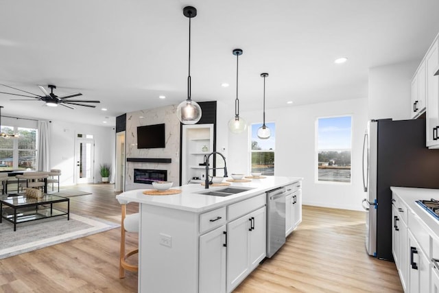 kitchen featuring appliances with stainless steel finishes, white cabinetry, sink, hanging light fixtures, and a center island with sink