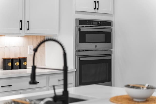 kitchen with white cabinets, backsplash, sink, and stainless steel double oven