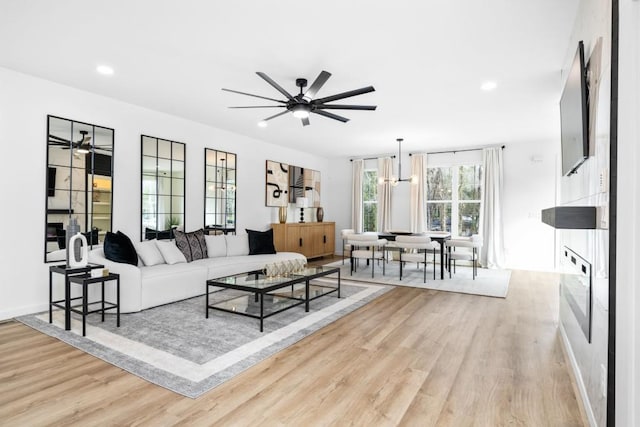 living room featuring a fireplace, ceiling fan with notable chandelier, and light hardwood / wood-style flooring