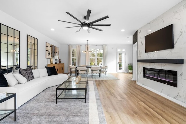 living room featuring light hardwood / wood-style flooring, ceiling fan with notable chandelier, and a fireplace