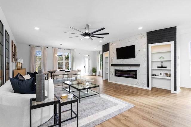 living room featuring ceiling fan with notable chandelier, a high end fireplace, built in features, and wood-type flooring