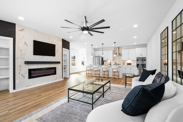 living room featuring built in features, a fireplace, light hardwood / wood-style floors, and ceiling fan