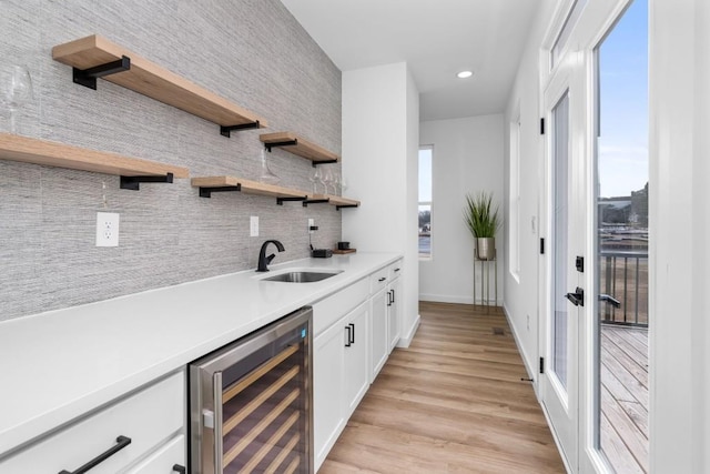 bar with sink, light hardwood / wood-style flooring, beverage cooler, decorative backsplash, and white cabinets