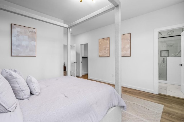 bedroom with a walk in closet, wood-type flooring, and connected bathroom