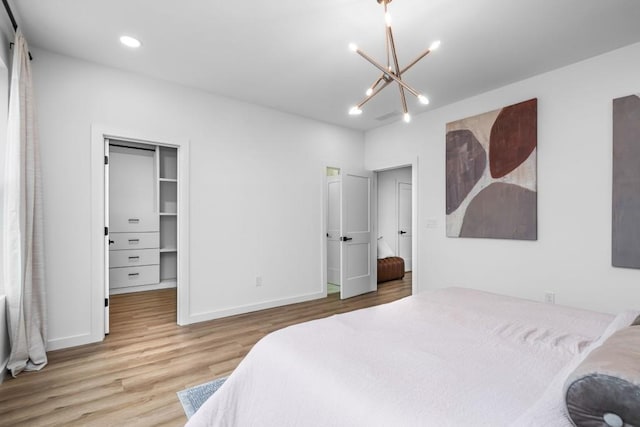 bedroom with an inviting chandelier, a walk in closet, and light hardwood / wood-style flooring