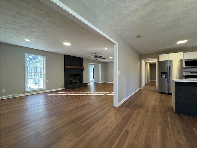 unfurnished living room with ceiling fan, dark hardwood / wood-style floors, a brick fireplace, and a textured ceiling