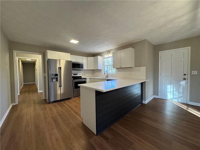 kitchen with white cabinetry, wood-type flooring, a textured ceiling, appliances with stainless steel finishes, and kitchen peninsula