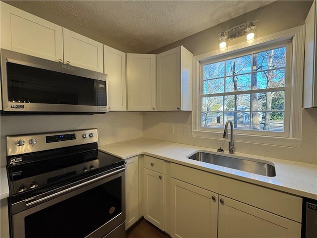 kitchen with appliances with stainless steel finishes, sink, a textured ceiling, and white cabinets