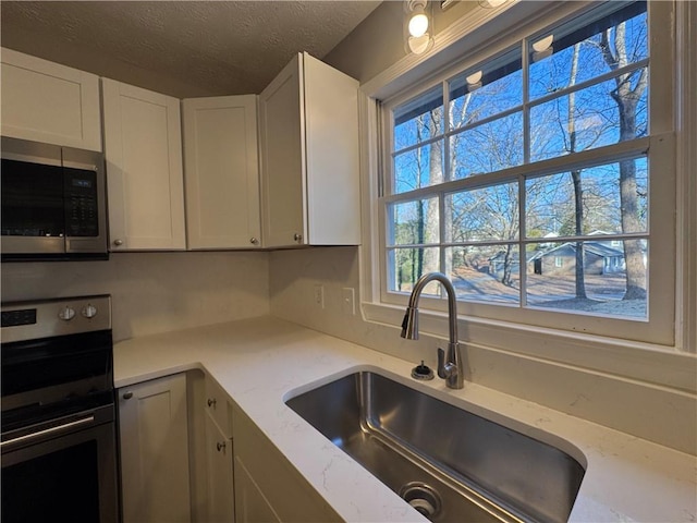 kitchen with sink, white cabinets, light stone counters, stainless steel appliances, and a textured ceiling