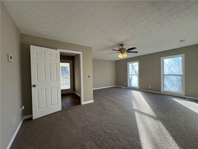 spare room with ceiling fan, a wealth of natural light, a textured ceiling, and dark colored carpet