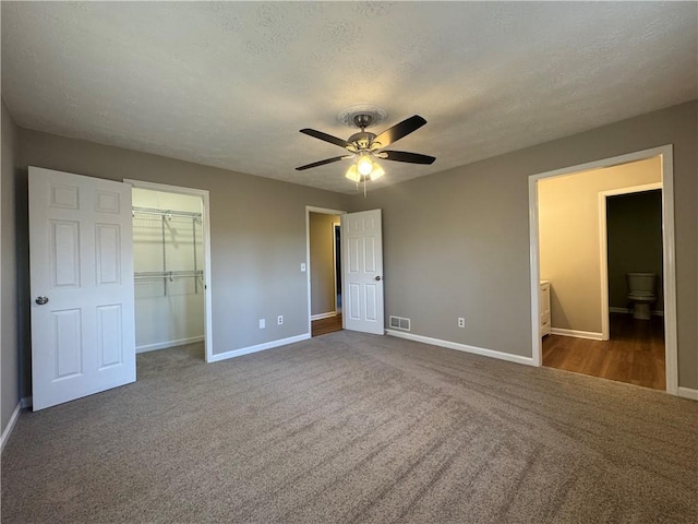 unfurnished bedroom with ceiling fan, ensuite bathroom, carpet, a textured ceiling, and a closet