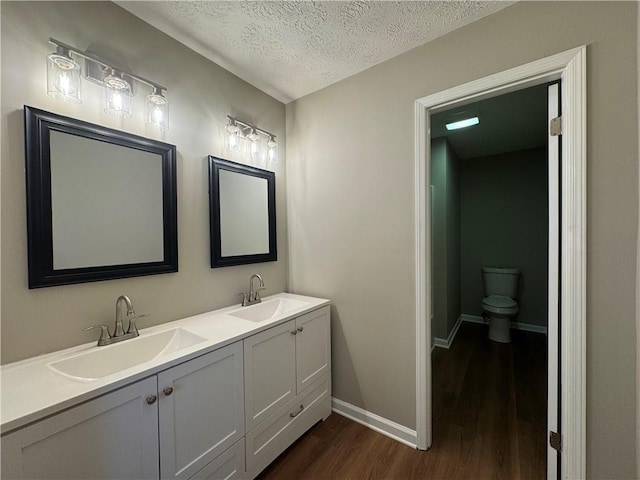 bathroom with hardwood / wood-style flooring, vanity, toilet, and a textured ceiling