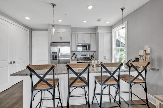 kitchen featuring a breakfast bar, visible vents, stainless steel appliances, and dark wood finished floors