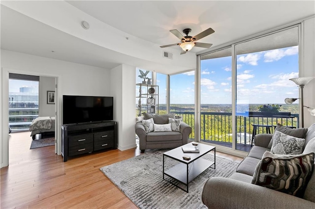 living room with a wealth of natural light, expansive windows, light hardwood / wood-style flooring, and ceiling fan