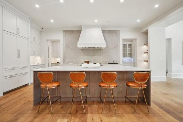 kitchen with a large island, a breakfast bar, white cabinets, and custom exhaust hood