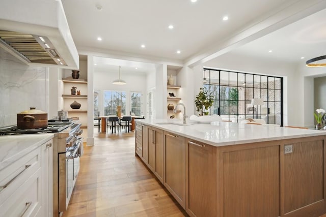 kitchen featuring sink, light stone counters, premium range hood, a spacious island, and double oven range