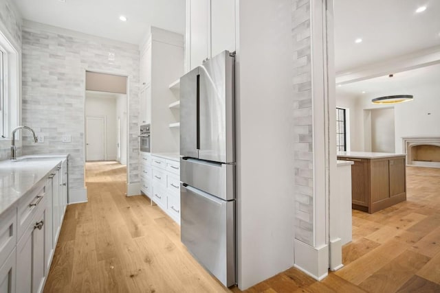 kitchen with appliances with stainless steel finishes, light wood-type flooring, light stone counters, sink, and white cabinetry