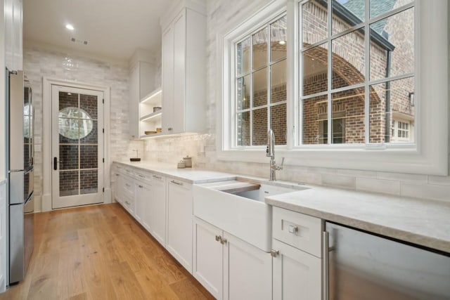 kitchen featuring stainless steel refrigerator, white cabinetry, sink, light stone countertops, and light wood-type flooring