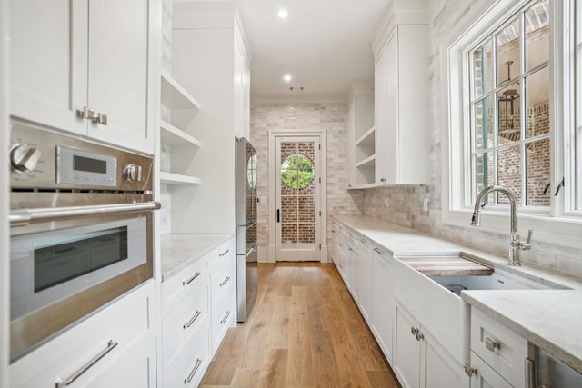 kitchen with light stone counters, stainless steel oven, white cabinets, and sink