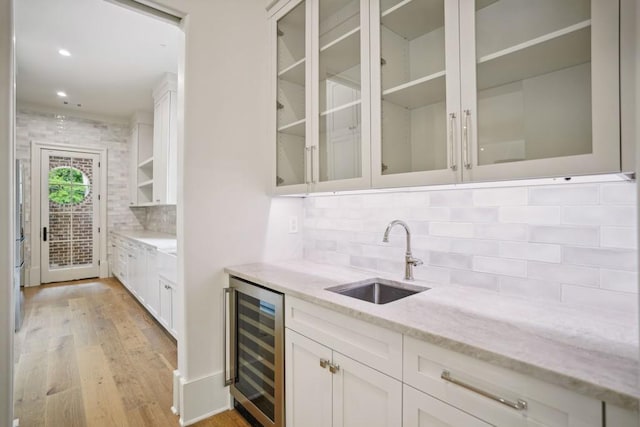 bar featuring decorative backsplash, light stone countertops, beverage cooler, sink, and white cabinetry