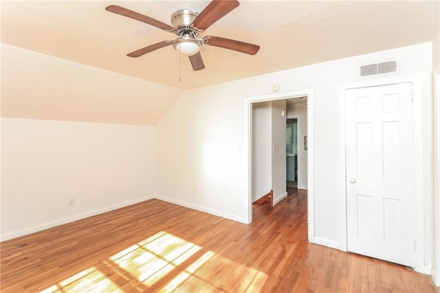 interior space with visible vents, light wood-style flooring, baseboards, ceiling fan, and vaulted ceiling