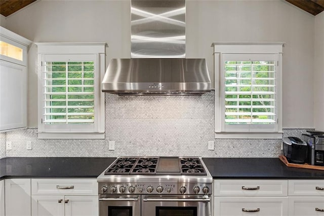 kitchen with white cabinets, vaulted ceiling, double oven range, wall chimney exhaust hood, and dark countertops