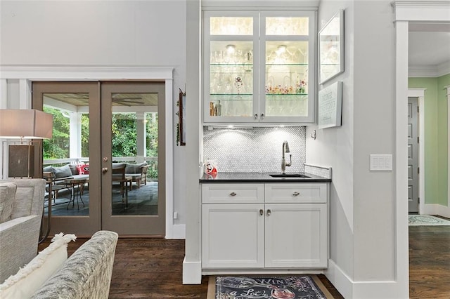 bar featuring french doors, dark wood-type flooring, a sink, and decorative backsplash