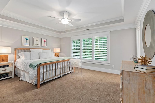 carpeted bedroom with baseboards, visible vents, ceiling fan, ornamental molding, and a tray ceiling