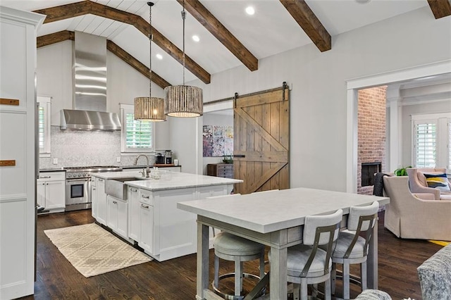 kitchen featuring a barn door, lofted ceiling with beams, wall chimney exhaust hood, high end stove, and a sink