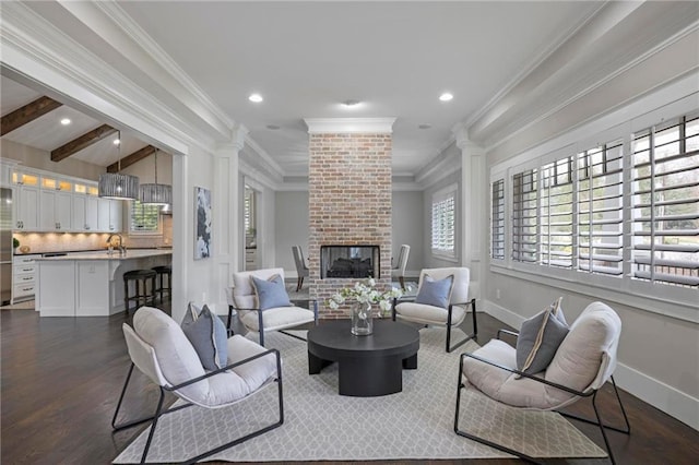 living room featuring dark wood-style flooring, baseboards, a brick fireplace, beamed ceiling, and crown molding