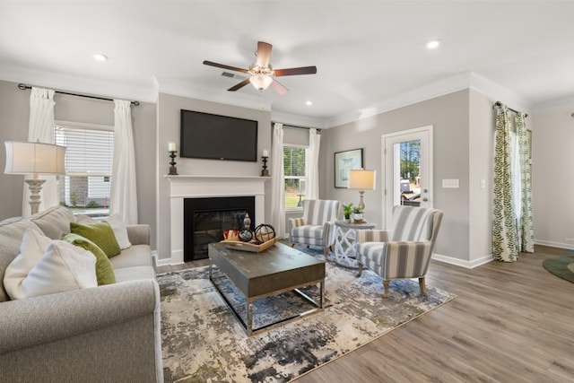 living area featuring baseboards, a glass covered fireplace, ornamental molding, wood finished floors, and recessed lighting