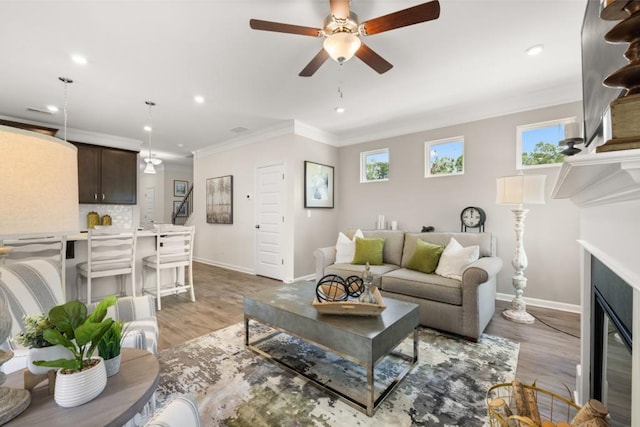 living area featuring baseboards, ornamental molding, a glass covered fireplace, and light wood-style floors