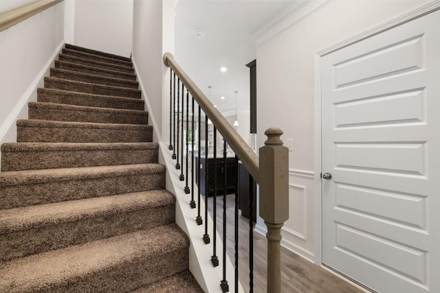 stairs with wainscoting, wood finished floors, and a decorative wall